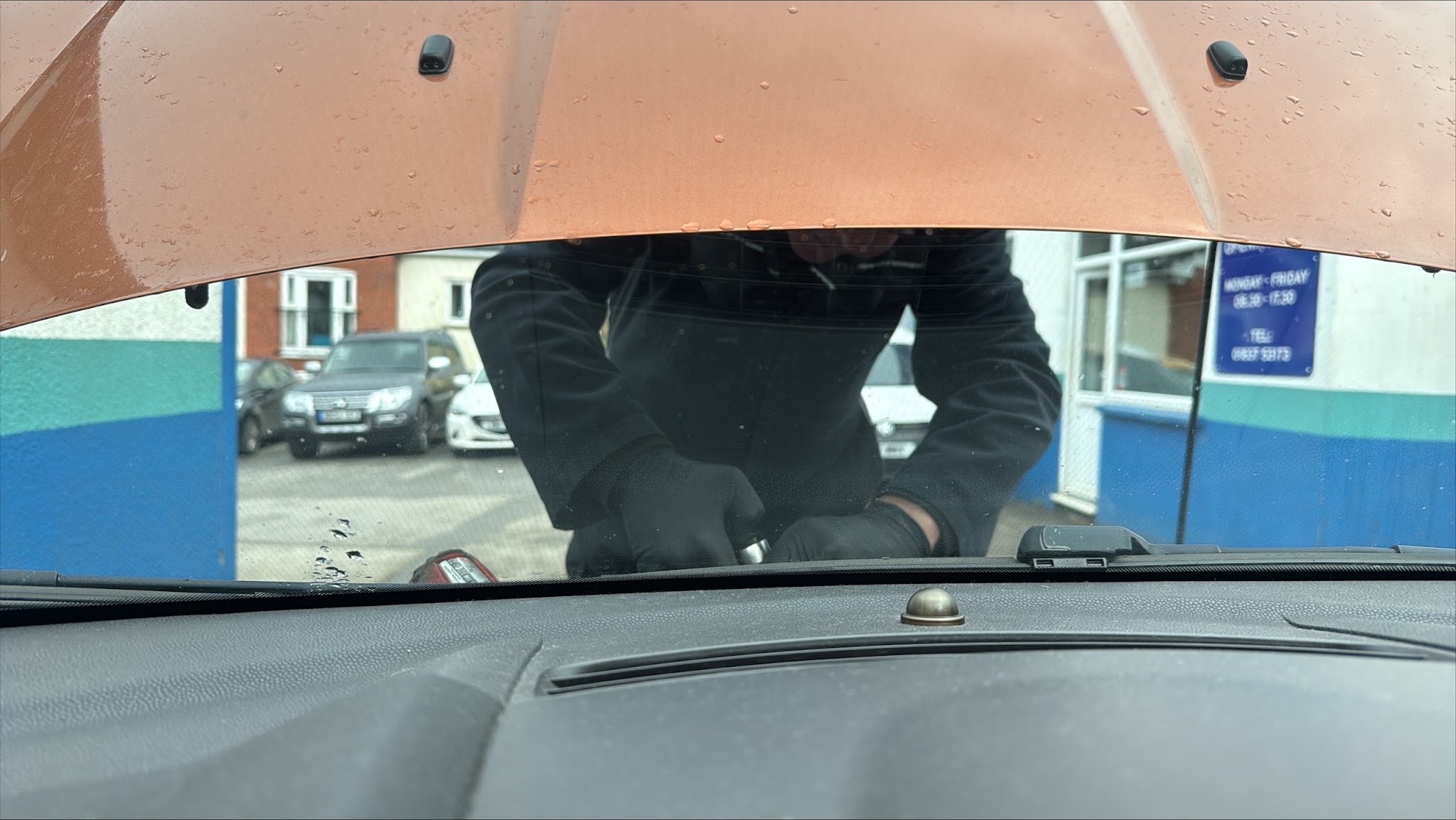 A mechanic in black gloves working under the open bonnet of a customer's car on the forecourt at Mill Road Garage